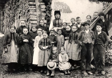 Albert Nyfeler, „Schulklasse in Kippel“, 1918 (Mediathek Wallis, Martigny). Die Fotografie zeigt Schulkinder mit ihrer Lehrerin vor dem mit 1665 datierten Meyerhaus am Kleinen Platz in Kippel.